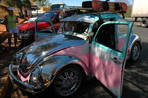 VW Bug, Made in the shade, chrome pink blue purple VW Bug, chrome wheels, hooded lamps, ski boards, stopped at a toil station, Highway 2 or 15, Mexico by Wonderlane