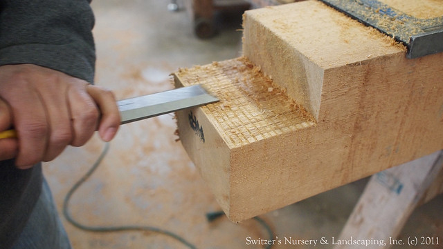 Using  a wood chisel to finish cleaning out the notch of a Real Cedar post for a Custom Classic Cedar Pergola.