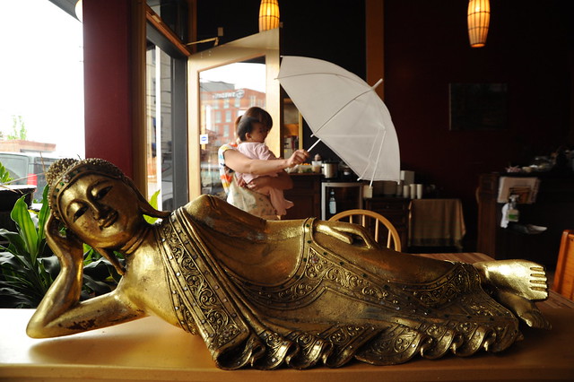 Reclining gold Thai Buddha, Sky Blue, a baby, enters with her friend carrying an auspicious white umbrella, UMA Thai restaurant, Ballard, Seattle, Washington, USA