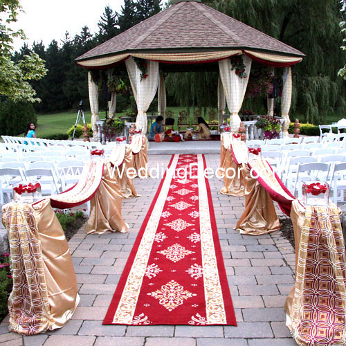 A wedding mandap in ivory and gold with a red aisle runner and piller 