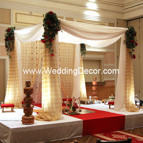 A wedding mandap in gold and ivory with red and gold aisle carpet and silk 