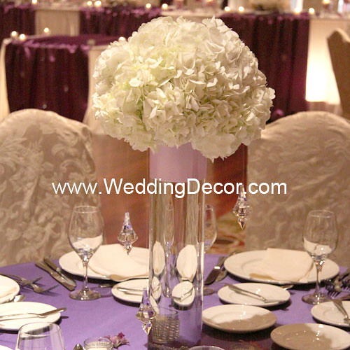 A wedding centerpiece in a cylindar vase with hydrangea flowers and hanging