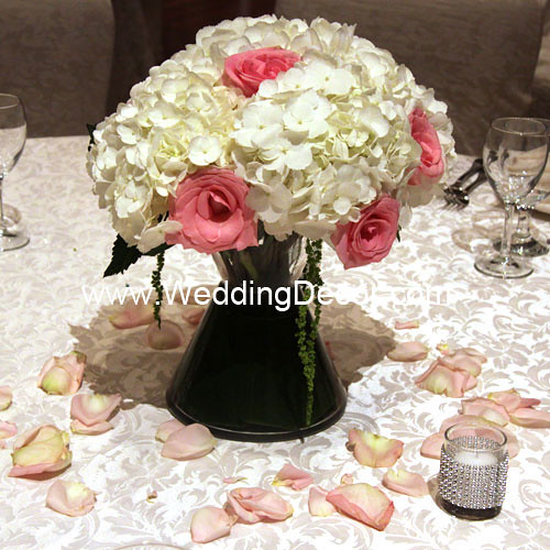 A wedding centerpiece in a bow tie vase with hydrangea flowers pink roses