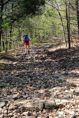 Picture showing a girl with a backpack hiking up a rocky hill trail in Piney Creek Wilderness in Missouri.
