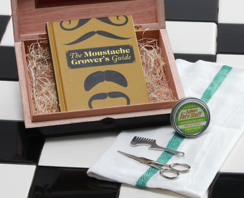 Steel mustache comb, mustache wax, stainless steel scissors, and a mustache growers guide in a reclaimed cigar box