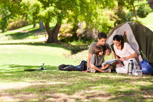 Family of four reading on the grass in front of a tent with tree in background. Photo courtesy of ThinkStock.