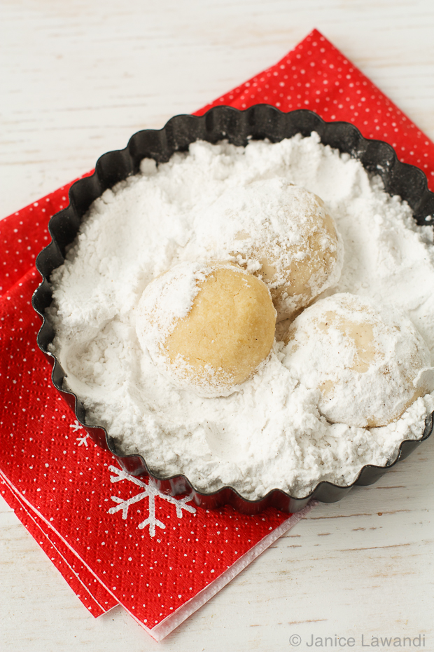 Coating snowball cookies in powdered sugar.