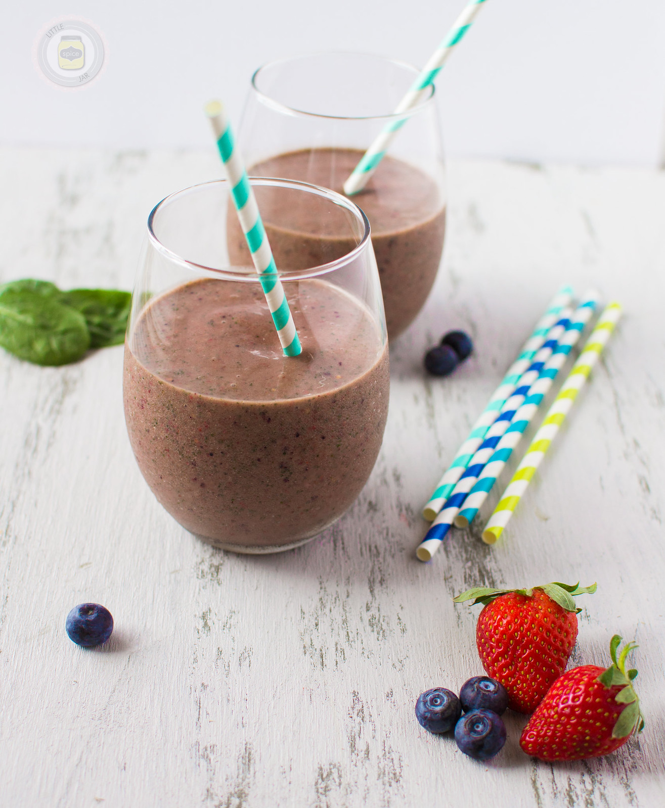 smoothie in stemless wine glasses on white surface with colorful striped straw and fresh berries