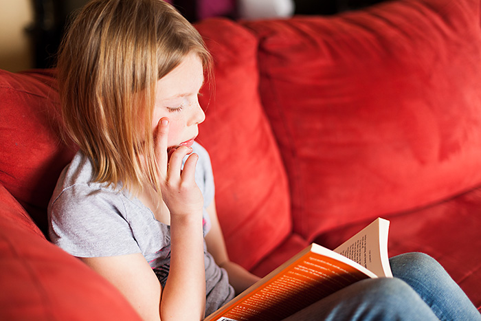 A 7 Year old reading on a red couch