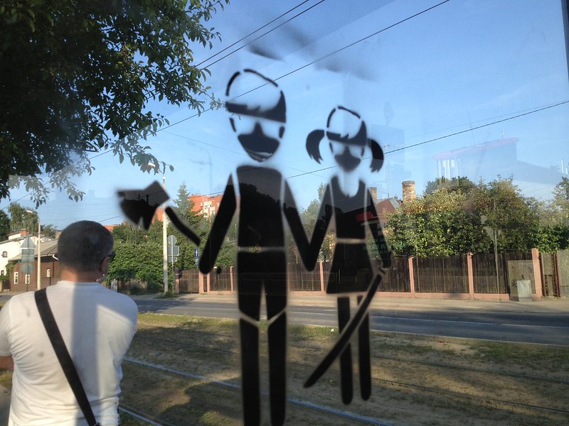 A gril and a boy holding an ax and a sword graffiti on a glass at a bus stop in Teika by aigarsbruvelis