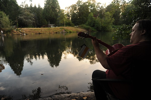 Billy breaks in Pinky, a new 3/4 size Washburn guitar with tags still attached, down by the Nisqually river, reflection of trees, summer evening, Nisqually, Washington, USA by Wonderlane