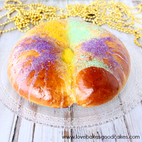 Traditional New Orleans King Cake on cake plate with gold beaded necklaces in background.