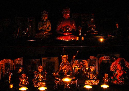 Buddhist Shrine lit with candles, from left to right, bottom to top, Vajra bell, Tara, Tara, Padmasambhava, Manjushri, Vajra Guruda, Zambala, Vajrayogini, Vajrayogini, Vajra Sattva, Amitabha Buddha / Gyalwa Gyamtso, vajra bell, Lord Buddha, Padmasambhava, by Wonderlane