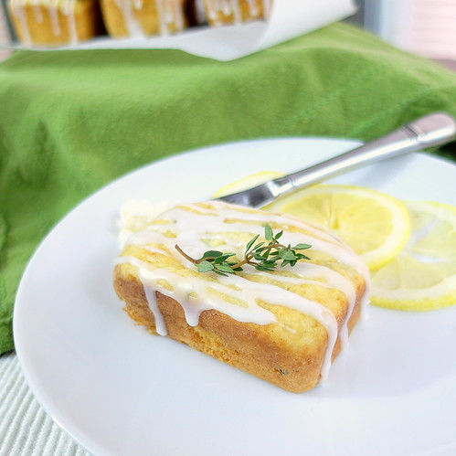 A single Lemon Thyme Tea Cake is on a white plate with lemon slice garnish and fresh thyme.