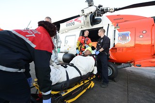 A Coast Guard MH-60 Jayhawk helicopter crew transfers an injured man to a Kodiak City Fire ambulance crew for further transfer to commercial medevac services in Kodiak, Alaska, Nov. 27, 2013. The man injured his head and right eye during a fall aboard the cargo vessel Sea Land Charger 550 miles south of Kodiak Nov. 26. U.S. Coast Guard photo by Petty Officer 3rd Class Diana Honings.