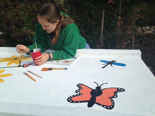 Image of a volunteer painting a monarch butterfly on a storm drain.