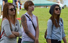Three young girls, high school students, standing together listening, one with large tatoo of tree on her arm.