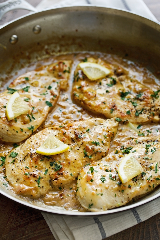 skillet with chicken in lemon garlic cream sauce topped with fresh lemon wedges