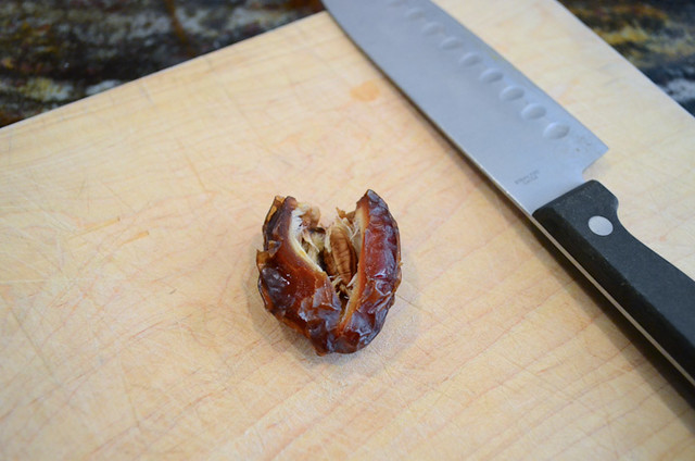 A date split open on a cutting board, revealing the pit that is in the center.
