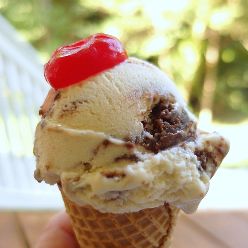Close up of a cake cone with a scoop of ice cream and a cherry on top.