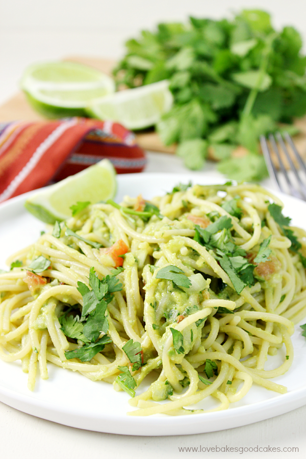 Guacamole Pasta on a white plate with limes and cilantro.