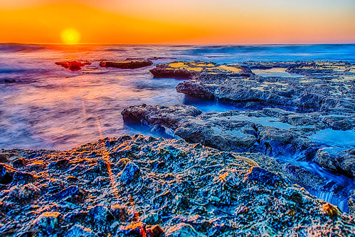 sunrise beach marine reserve rocks ocean sunflare orange blue