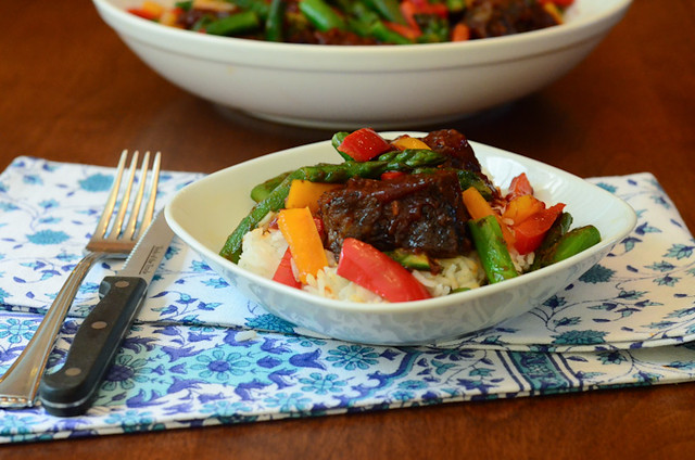 A white serving dish with white rice and Asian BBQ Ribs over white rice with stir fry vegetables.