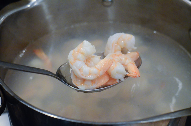 A spoon lifts some cooked shrimp out of a pot.