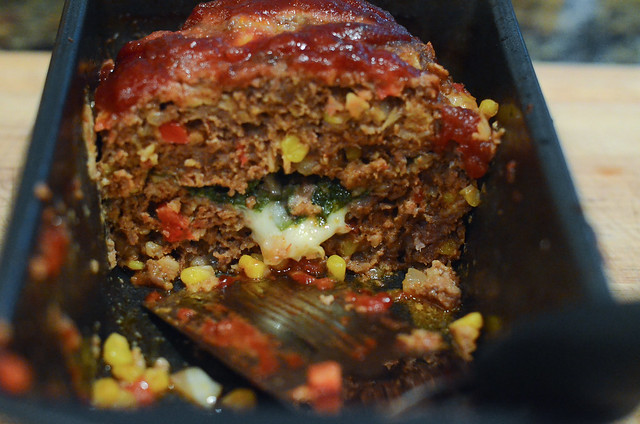 A close up of a meatloaf sliced open to reveal cheese and vegetables.