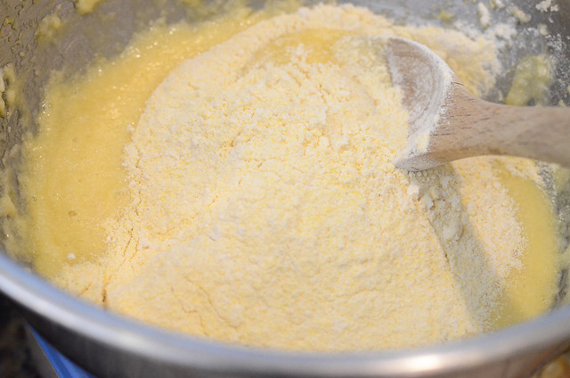 A spoon stirs flour and cornmeal in a bowl.
