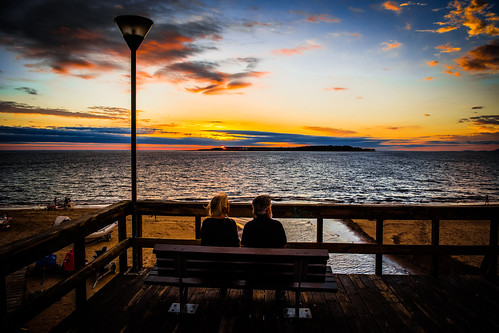 ocean sunset people sun beach water clouds bench lights couple colours
