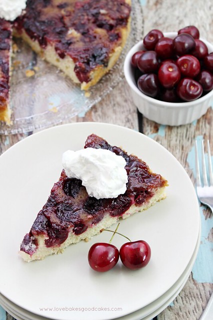 Cherry Upside Down Cake with Almond Whipped Cream on a plate with cherries.