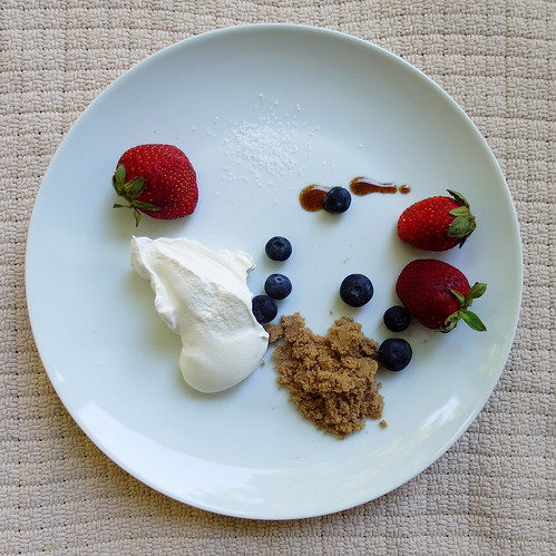 A white plate with fresh strawberries, blueberries, brown sugar and a dollop of Fruit Dip Ice Cream.