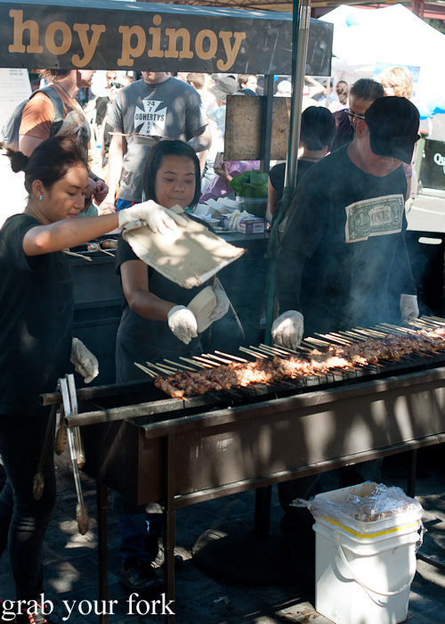 Fanning the charcoal barbecue of chicken skewers at Hoy Pinoy, Queen Victoria Market, Melbourne