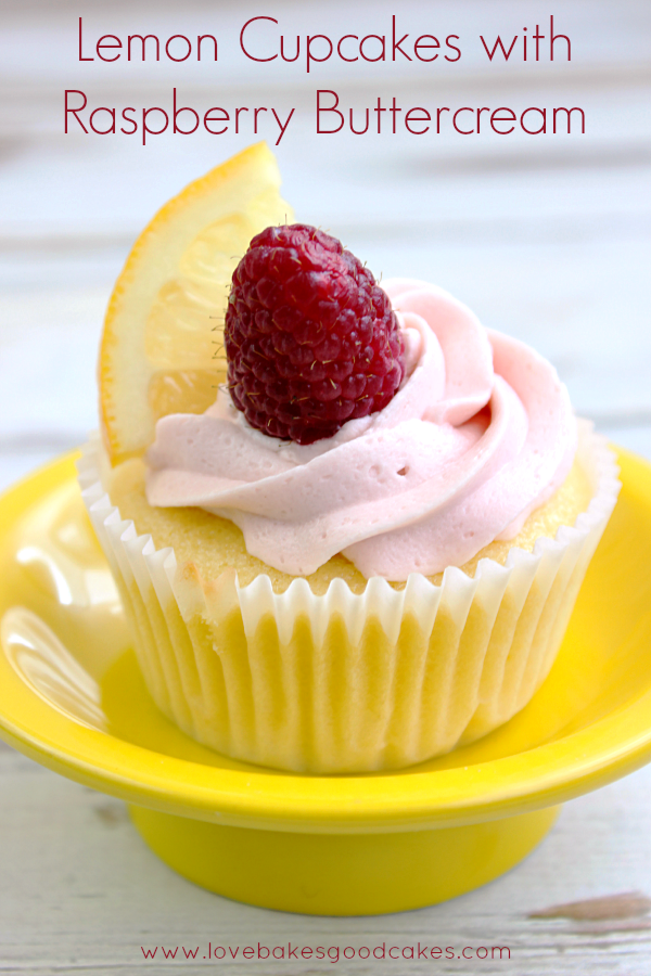 Lemon Cupcakes with Raspberry Buttercream in a yellow dish with a slice of lemon and a raspberry on top.