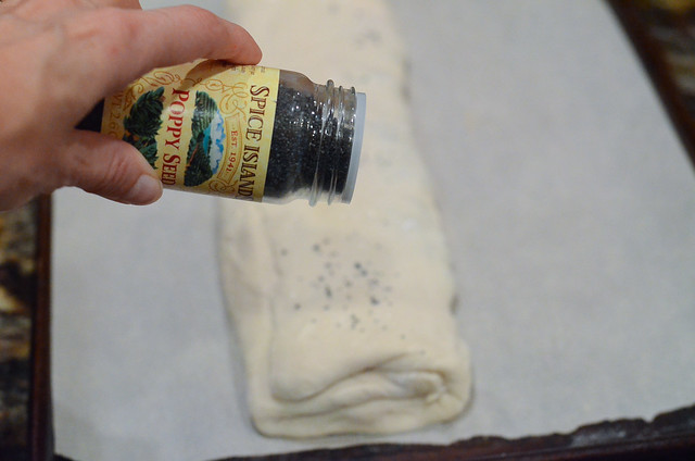 A bottle of poppy seeds hovering over stuffed bread.