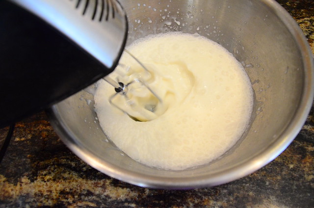 Whole milk and cream of coconut being mixed together in a bowl with a hand mixer.