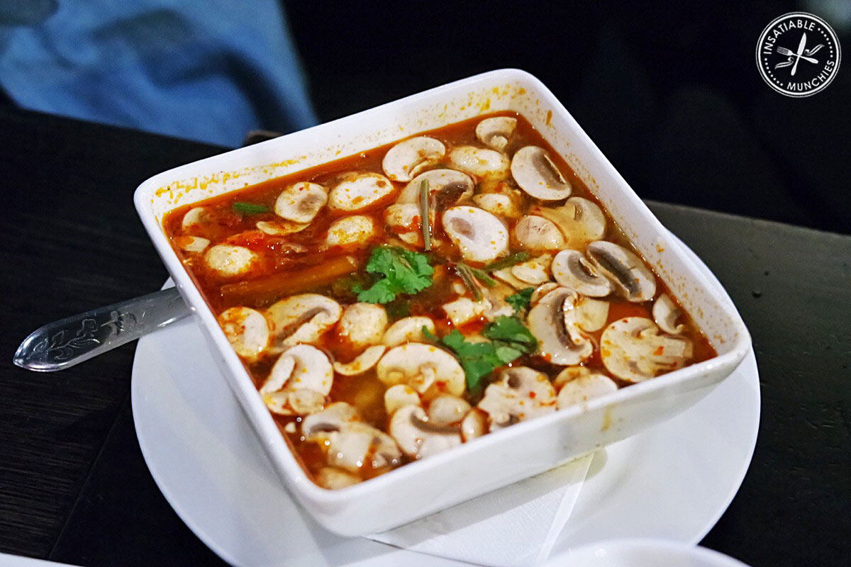 Tom Yum Goong - a hot and sour prawn soup that's flavoured with lime and lemongrass - sits in a large square bowl with button mushrooms and garnished with coriander.