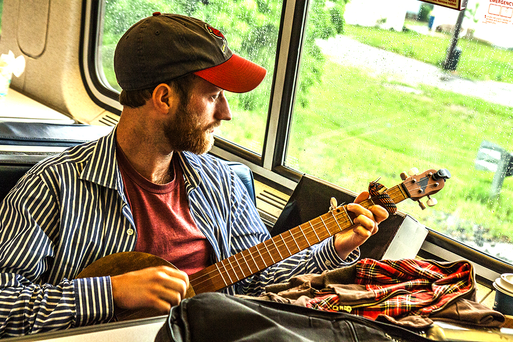 Man-playing-five-stringed-guitar-in-train's-lounge-car--Indiana