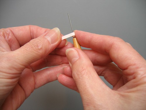 hands holding a quilling needle tool with rolled coil