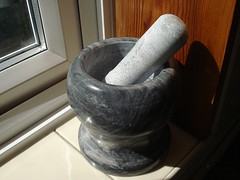 A substantial grey-stone pestle and mortar sitting on a tiled windowsill.