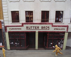 A model of a double-fronted terraced shop with a sign reading “Rutter Bros / Furnishing Specialists”.