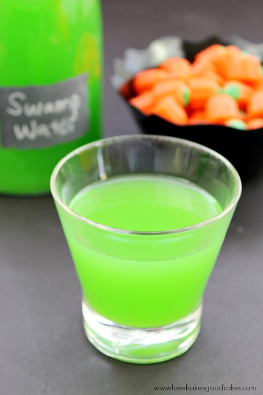 Swamp Water Drink in a clear glass with a bowl of candy pumpkins.