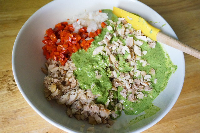 Chicken, onion, red pepper, and cilantro sauce, just barely begun to be mixed in a large white bowl