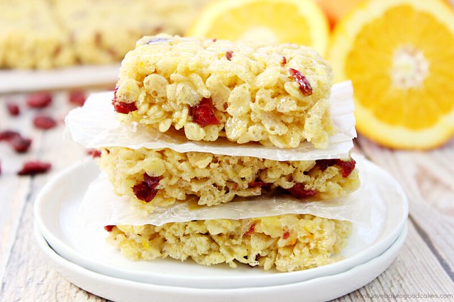 Cranberry Orange Crispy Treats stacked on a white plate with oranges.