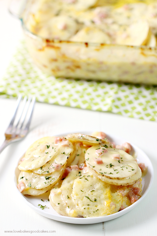 Cheesy Scalloped Potatoes with Ham in a casserole dish and on a white plate with a fork.