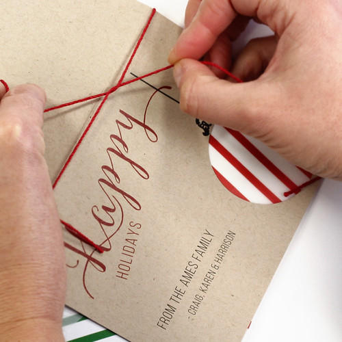 hands tying red twine around spine of printed holiday card