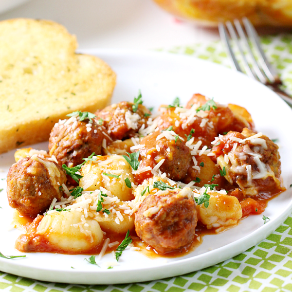 Gnocchi and Meatball Bake on a white plate with garlic bread and a fork close up.