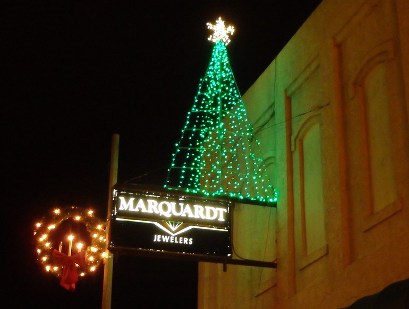 wreath on a utility pole next to Marquardt Jewelers sign with a tree made from green light strings