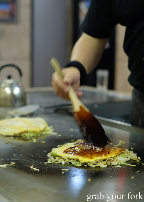 Brushing okonomiyaki sauce on our Hiroshima-style okonomiyaki at Okonomimura, Hiroshima
